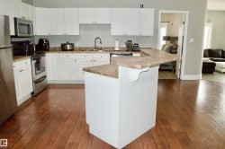 Kitchen featuring white cabinetry, wood-finish flooring, stainless steel appliances, a corner sink with a gooseneck faucet, and a peninsula countertop with seating overhang - 