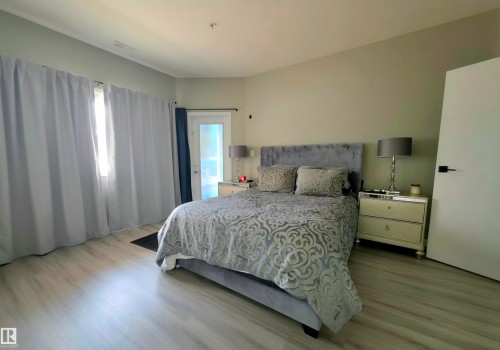 Spacious room featuring light wood-finish flooring, neutral wall tones, and a glass-paneled exterior door - 104 4312 139 Avenue, Edmonton, AB 