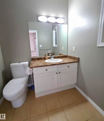 Bathroom featuring a white vanity with cabinet storage, a speckled countertop, an integrated sink, and a large wall-mounted mirror - 104 4312 139 Avenue, Edmonton, AB 