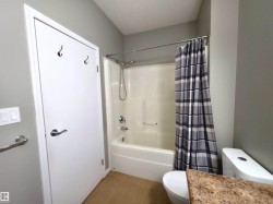 Bathroom featuring a white tub/shower combination with a chrome showerhead, tan tile flooring, a white toilet, and a vanity with a light-colored countertop - 