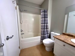 Bathroom featuring a white bathtub and shower combination with chrome fixtures, a toilet, a white vanity with a tan countertop, and light-toned floor tiling - 