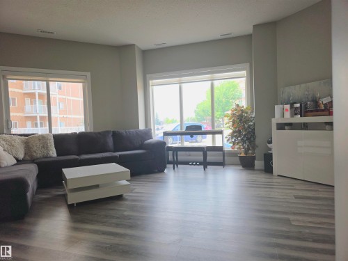 Spacious living area featuring large windows, wood-finish flooring, and neutral wall tones - 104 4312 139 Avenue, Edmonton, AB 