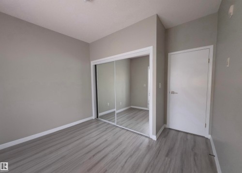 Neutral gray wall tones with white trim, wood-finish flooring, and mirrored closet doors - 104 4312 139 Avenue, Edmonton, AB 