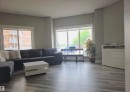Spacious living area featuring large windows, light gray wall paint, wood-finish flooring, white window trim, and a built-in white cabinet - 104 4312 139 Avenue, Edmonton, AB 