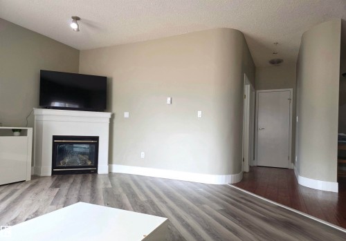 Living area featuring a white mantel fireplace, wood-finish flooring, and a curved wall architectural detail - 104 4312 139 Avenue, Edmonton, AB 