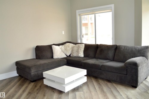Spacious living area featuring wood-finish flooring, neutral wall tones, and a sliding glass door leading to an outdoor balcony - 104 4312 139 Avenue, Edmonton, AB 