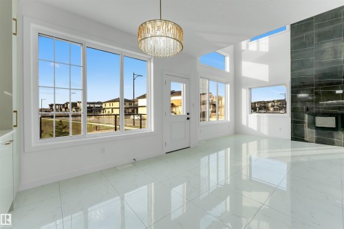 Bright living area featuring high ceilings, large windows, a contemporary chandelier, a built-in fireplace with a dark tile surround, and light-colored tile flooring - 1536 64 Ave, Rural Leduc County, AB 