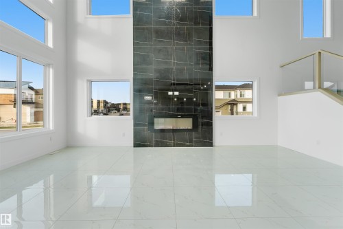 Two-story living area featuring a dark tile fireplace surround with an electric fireplace, high ceilings, large windows, and reflective light-toned floor tiling - 1536 64 Ave, Rural Leduc County, AB 