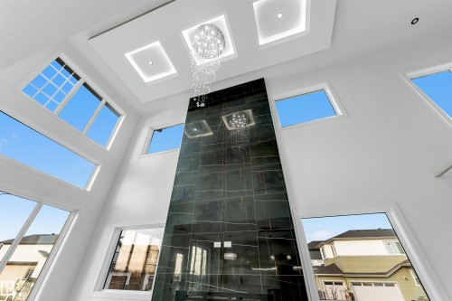 Two-story great room featuring a dark tiled fireplace, a tiered crystal chandelier, and multiple large windows - 1536 64 Ave, Rural Leduc County, AB 