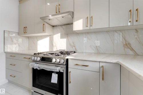 Contemporary kitchen featuring white cabinetry with gold-tone hardware, a stainless steel range with a matching range hood, and a marble-look backsplash and countertops - 1536 64 Ave, Rural Leduc County, AB 