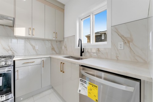 Contemporary kitchen featuring light-toned cabinetry with gold-toned hardware, a stainless steel gas range, and a stainless steel dishwasher - 1536 64 Ave, Rural Leduc County, AB 