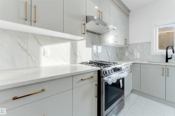Modern kitchen featuring white cabinetry with gold-tone hardware, white countertops, and a full backsplash with subtle veining - 