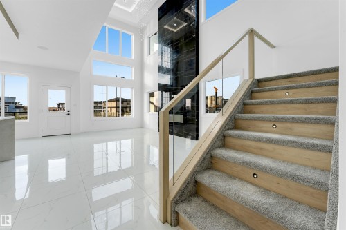 Open-concept foyer featuring white tile flooring and a modern staircase with carpeted treads and wood-finish risers - 1536 64 Ave, Rural Leduc County, AB 