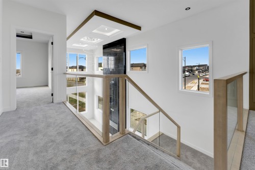 Modern interior balcony featuring glass railings with light wood-finish accents, grey carpet flooring, and a contemporary light fixture - 1536 64 Ave, Rural Leduc County, AB 
