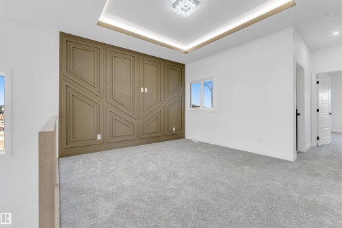 Spacious room featuring a decorative accent wall with geometric paneling, tray ceiling with cove lighting, and a contemporary flush mount light fixture - 1536 64 Ave, Rural Leduc County, AB 