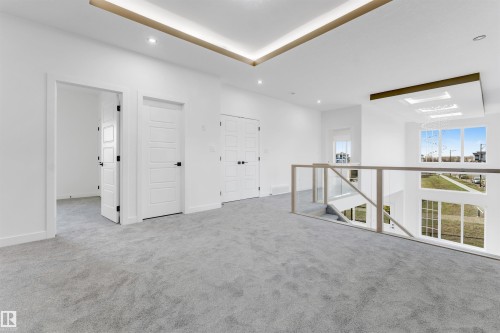 Upper-level landing featuring light gray carpet flooring, multiple white paneled doors with black hardware, and a glass-paneled railing overlooking an expansive window wall - 1536 64 Ave, Rural Leduc County, AB 