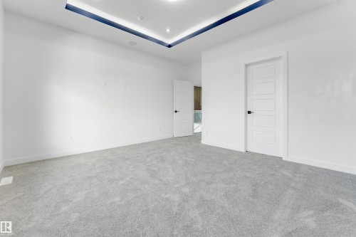 Spacious room featuring light gray carpeting, white walls, and a contemporary tray ceiling with recessed lighting and a blue accent stripe - 1536 64 Ave, Rural Leduc County, AB 