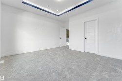 Spacious room featuring light gray carpeting, white walls, and a contemporary tray ceiling with recessed lighting and a blue accent stripe - 