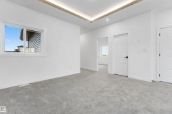Spacious room featuring light gray carpet flooring, a white trim window, and multiple panel doors with matte black hardware - 
