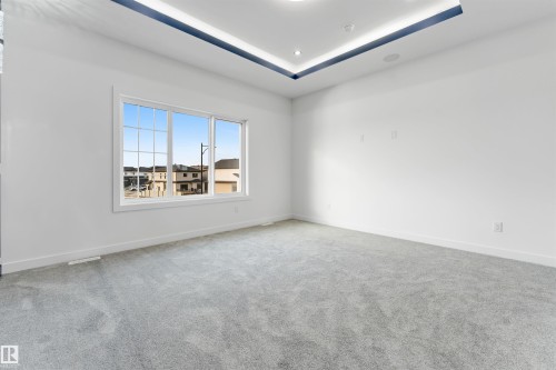 Spacious room featuring light gray carpeting, a large window with white trim, and a tray ceiling with recessed lighting - 1536 64 Ave, Rural Leduc County, AB 