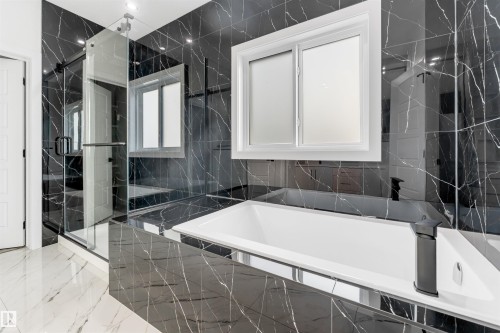 Soaking tub with a matte black faucet, surrounded by black marble-patterned tile, a white-framed window, and a glass-enclosed shower - 1536 64 Ave, Rural Leduc County, AB 