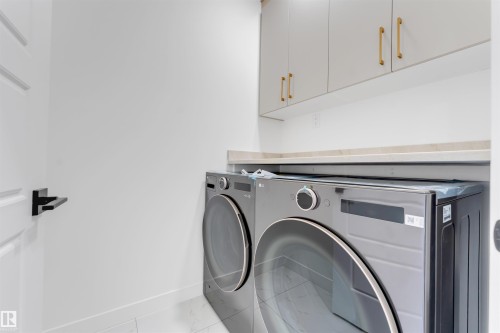 Dedicated laundry space featuring a white door with a black lever handle, built-in upper cabinetry with gold-tone hardware, and a light-toned countertop - 1536 64 Ave, Rural Leduc County, AB 