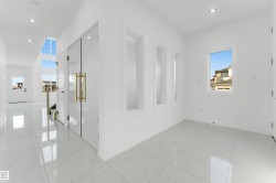 Bright interior space featuring large format tile flooring, recessed ceiling lighting, a clear glass entry door with brass hardware, and multiple window openings - 