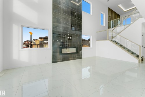 Spacious interior featuring high ceilings, large format polished tile flooring, a modern fireplace with a dark tile surround, and a contemporary staircase with glass panel railings - 1536 64 Ave, Rural Leduc County, AB 