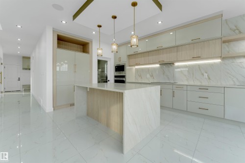 Modern kitchen featuring a large central island with a slatted wood-finish panel, integrated appliances, and a light-toned countertop - 1536 64 Ave, Rural Leduc County, AB 