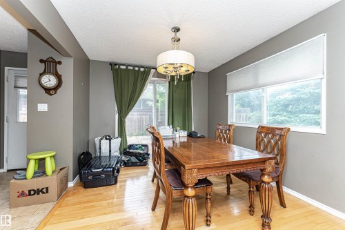 Dining area featuring wood-finish flooring, a contemporary chandelier, large window with roller shade, and sliding glass door - 11512 24 Avenue, Edmonton, AB 