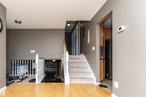 Hardwood flooring extending through the main level, staircase with wood banister and carpeted treads, and a lower level featuring a stone-surround fireplace - 11512 24 Avenue, Edmonton, AB 
