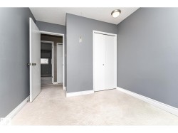 Bedroom featuring a neutral gray wall color, textured light-toned carpet, white bi-fold closet doors, white baseboards, and a flush-mount ceiling light - 