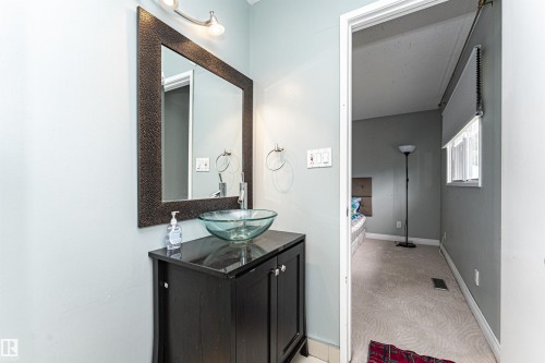 Bathroom vanity featuring a vessel sink, dark wood-finish cabinet, wall-mounted lighting, and a large framed mirror - 11512 24 Avenue, Edmonton, AB 
