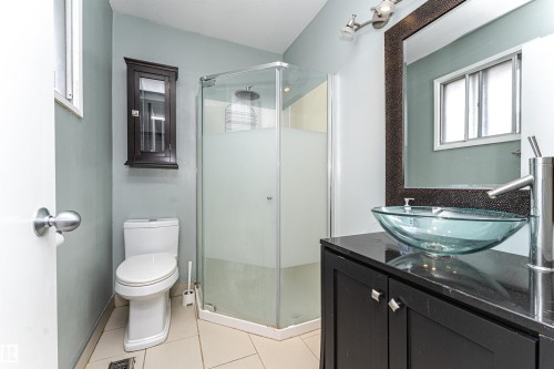 Modern bathroom featuring a contemporary glass vessel sink and dark wood-finish vanity with a stone countertop - 11512 24 Avenue, Edmonton, AB 