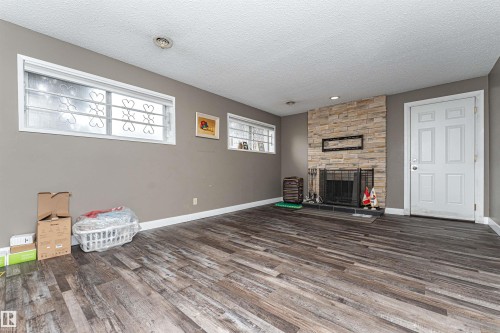 Spacious room featuring wood-finish flooring, a stacked stone fireplace with a black hearth, and multiple windows - 11512 24 Avenue, Edmonton, AB 