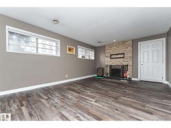 Spacious room featuring wood-finish flooring, a stone-clad fireplace with a black hearth, and multiple windows with decorative security bars - 