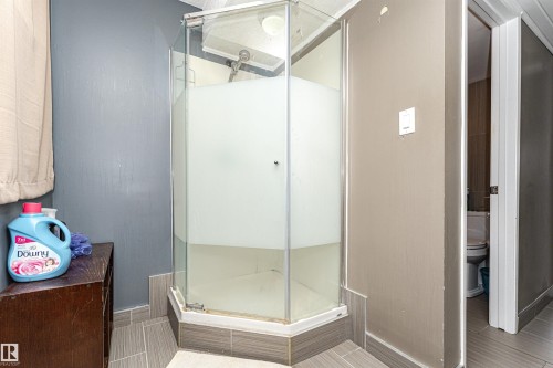 Corner shower enclosure with clear and frosted glass panels, featuring a tiled base and light gray flooring - 11512 24 Avenue, Edmonton, AB 