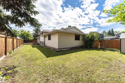 Expansive fenced backyard featuring a wooden deck, mature trees, and a utility shed - 11512 24 Avenue, Edmonton, AB 