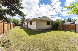 Expansive fenced backyard featuring a wooden deck, mature trees, and a utility shed - 