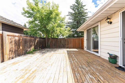 Exterior deck featuring a wood fence, mature trees, and sliding glass patio doors with screens - 11512 24 Avenue, Edmonton, AB 