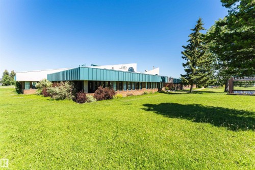 Expansive green lawn surrounds a commercial building featuring a brick base, horizontal windows, a teal-colored facade, and a white upper structure - 11512 24 Avenue, Edmonton, AB 
