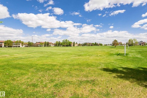 Expansive green space featuring a large grassy field, distant residential structures, and mature trees under a bright sky - 11512 24 Avenue, Edmonton, AB 
