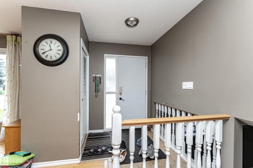 Foyer featuring a white entry door with a frosted sidelight, a louvered bi-fold closet, and a stair railing with a natural wood-finish top rail and white spindles - 11512 24 Avenue, Edmonton, AB 