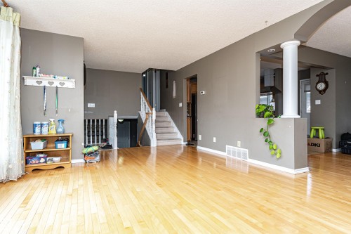 Spacious interior featuring light wood-finish flooring throughout, a traditional staircase with white risers and handrails, and a half-wall with a decorative column - 11512 24 Avenue, Edmonton, AB 