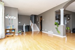 Spacious interior featuring light wood-finish flooring throughout, a traditional staircase with white risers and handrails, and a half-wall with a decorative column - 