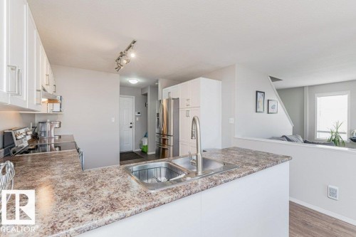 Kitchen featuring white cabinetry with silver hardware, dual basin stainless steel sink with a high-arc faucet, speckled countertop, and stainless steel refrigerator - 1816 36 Avenue, Edmonton, AB 