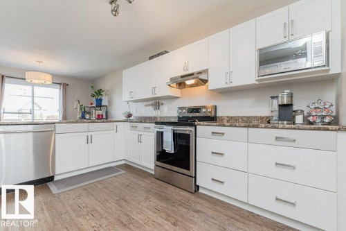 Kitchen featuring white cabinetry, stainless steel appliances, wood-finish flooring, and a window above the sink - 1816 36 Avenue, Edmonton, AB 