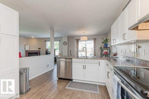Kitchen featuring white cabinetry, stainless steel appliances, wood-finish flooring, a stainless steel sink with a high-arc faucet, and granite-look countertops - 1816 36 Avenue, Edmonton, AB 