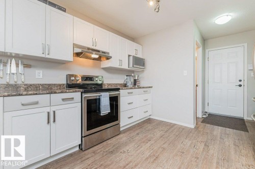 Modern kitchen featuring white cabinetry, stone-look countertops, stainless steel appliances, and wood-finish flooring - 1816 36 Avenue, Edmonton, AB 