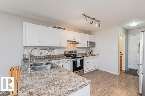 Contemporary kitchen featuring white cabinetry, a stainless steel double basin sink, and wood-finish flooring - 1816 36 Avenue, Edmonton, AB 